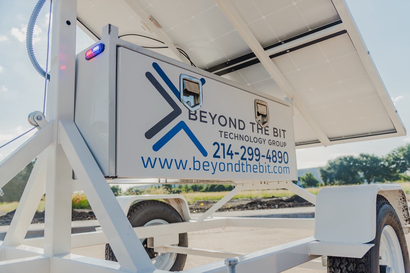 Close view of the Beyond the Bit equipment cabinet with the company name and phone number, the red-and-blue strobe lit on the cabinet corner, and the mast winch and cable beside it.
