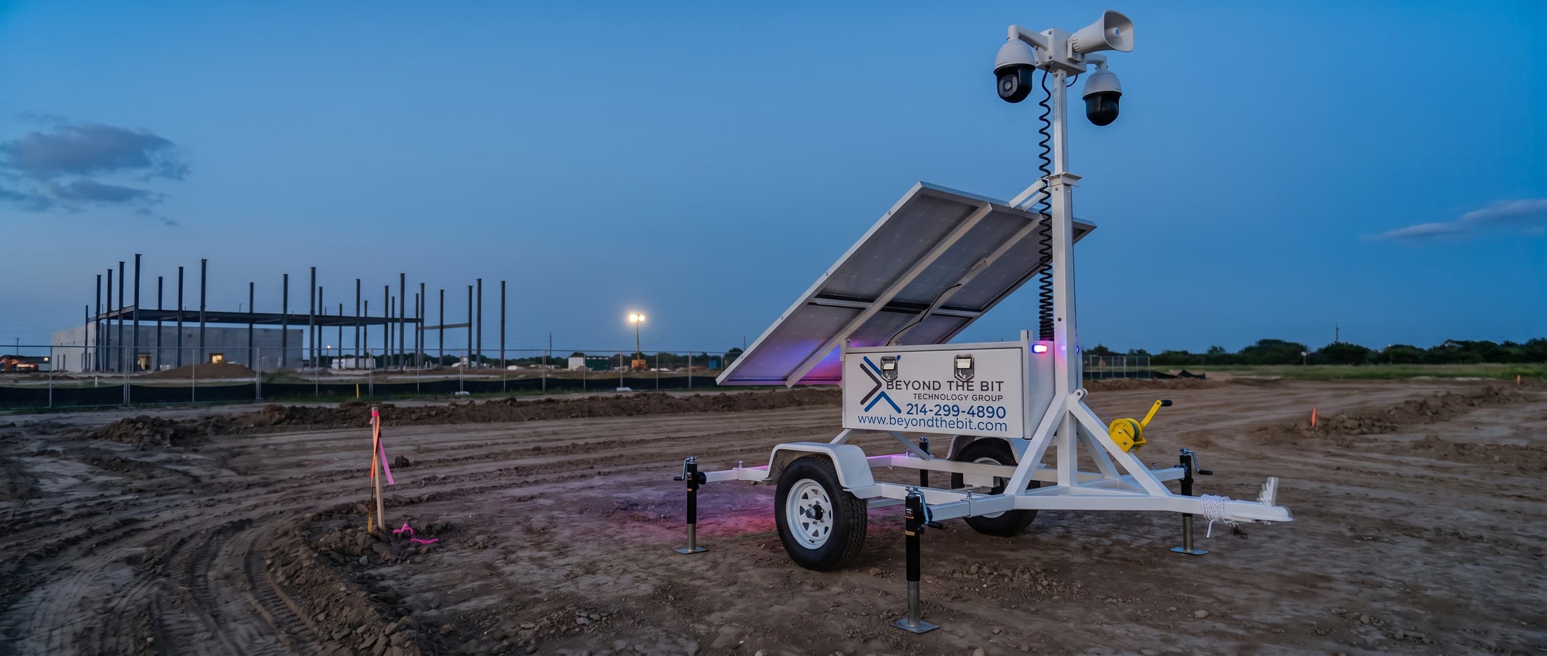A Beyond the Bit security trailer standing on a gravel pad at dusk with its camera mast raised, the kind of placement a site quote is built around.