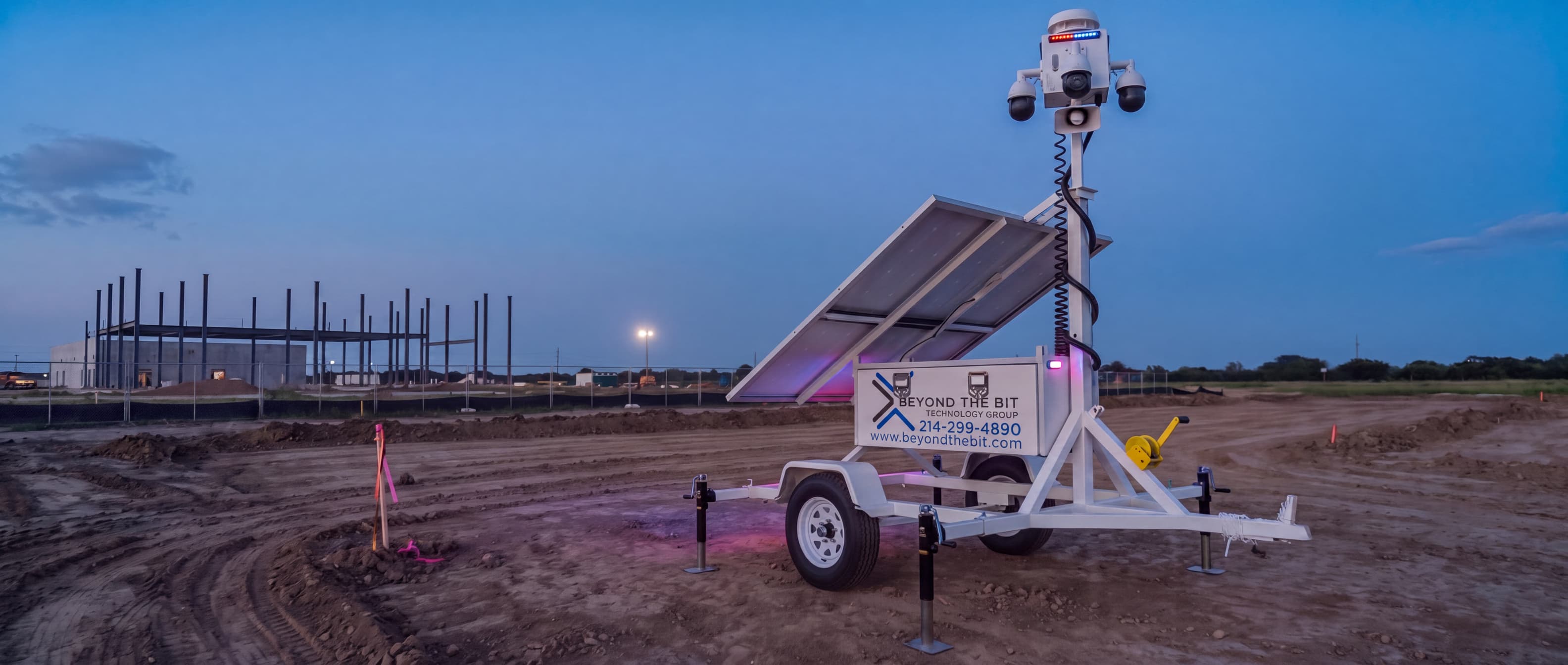 A Beyond the Bit security trailer standing on a gravel pad at dusk with its camera mast raised, the kind of placement a site quote is built around.