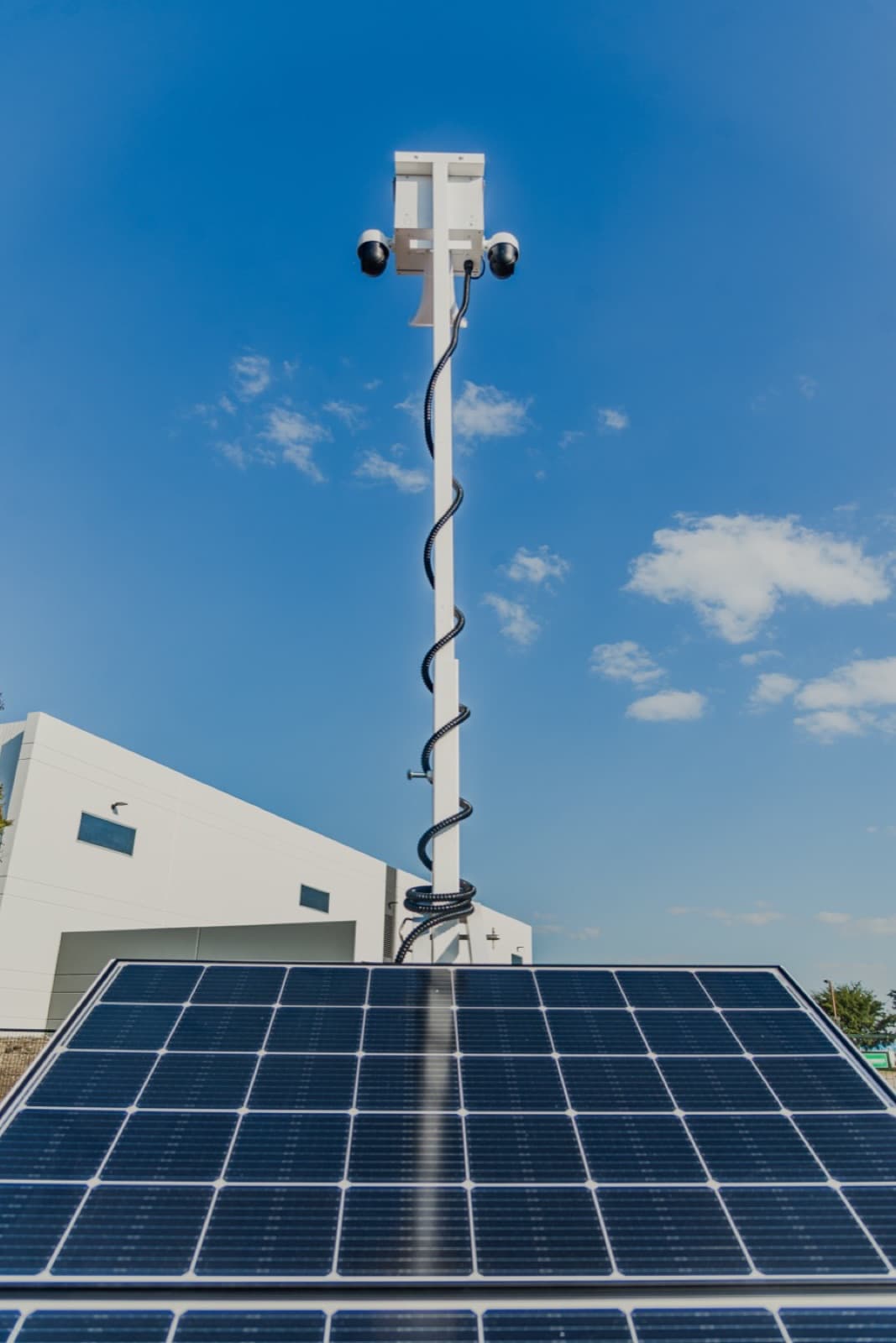 The two-section solar array of a Beyond the Bit security trailer seen from the panel face looking up the mast to the camera head, blue sky behind.