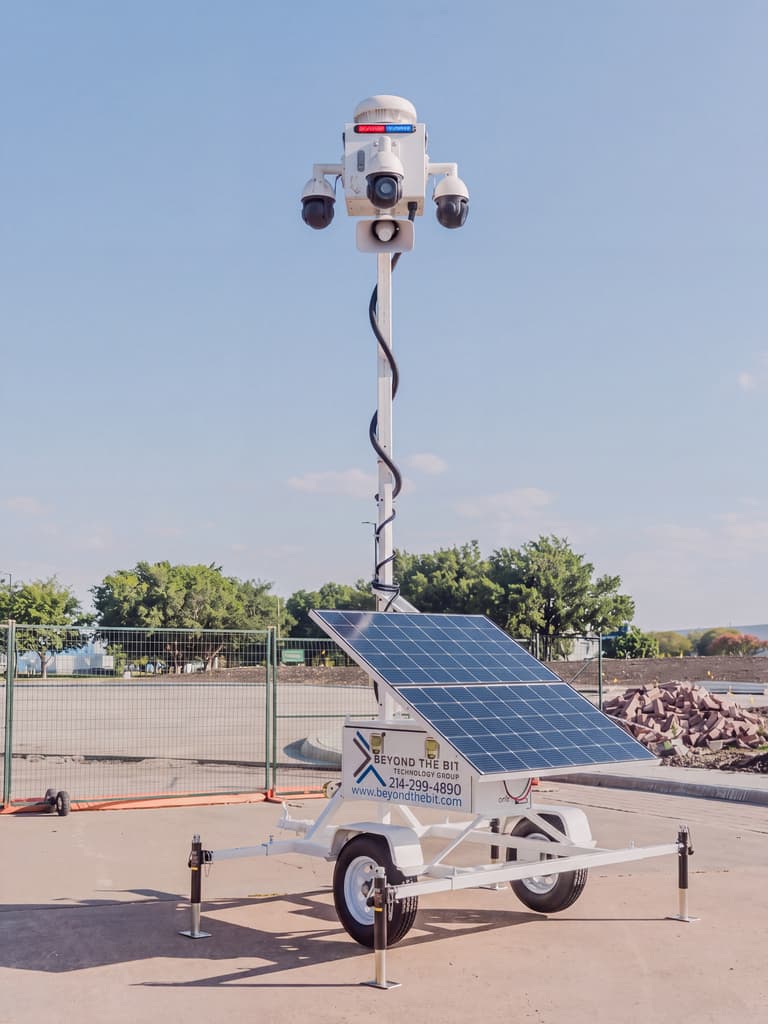 A white Beyond the Bit security trailer deployed on a jobsite pad in daylight, camera mast fully raised and solar array visible.
