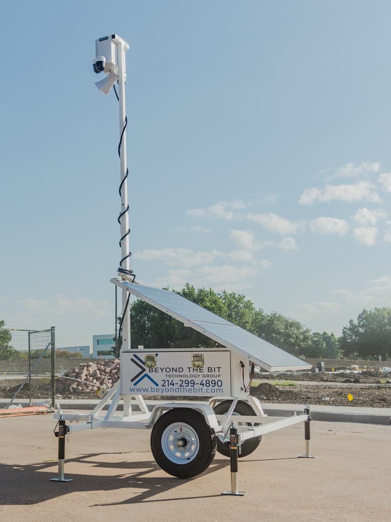 A white Beyond the Bit security trailer deployed on a jobsite pad in daylight, camera mast fully raised and solar array visible.